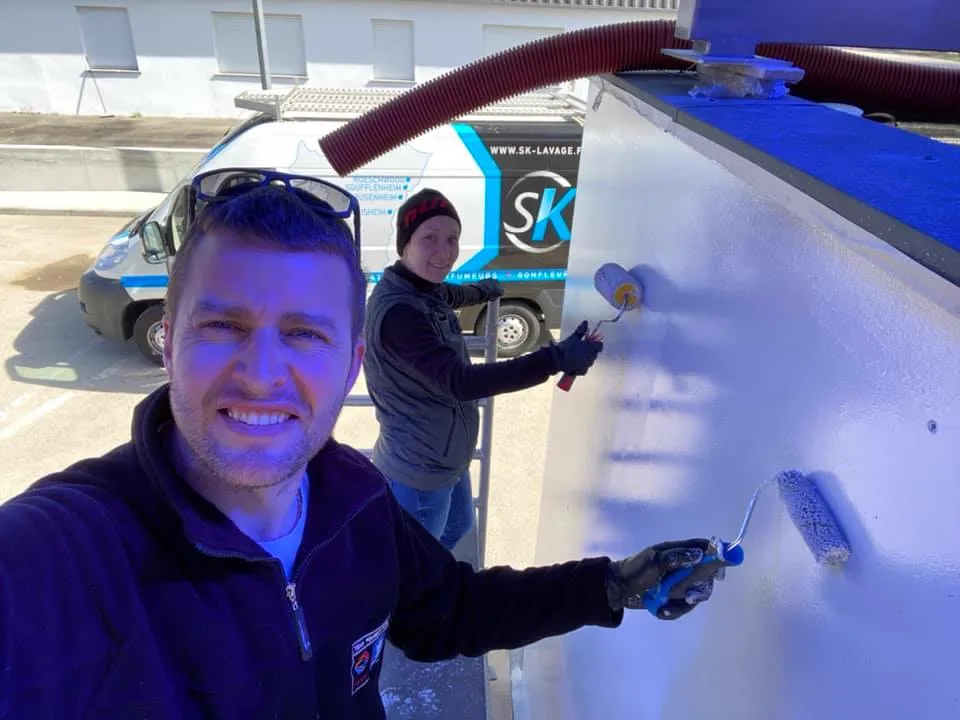 Monsieur Olivier Kientz et une autre personne de SK Lavage en train de peindre une surface avec des rouleaux et un camion de SK Lavage en arrière-plan.